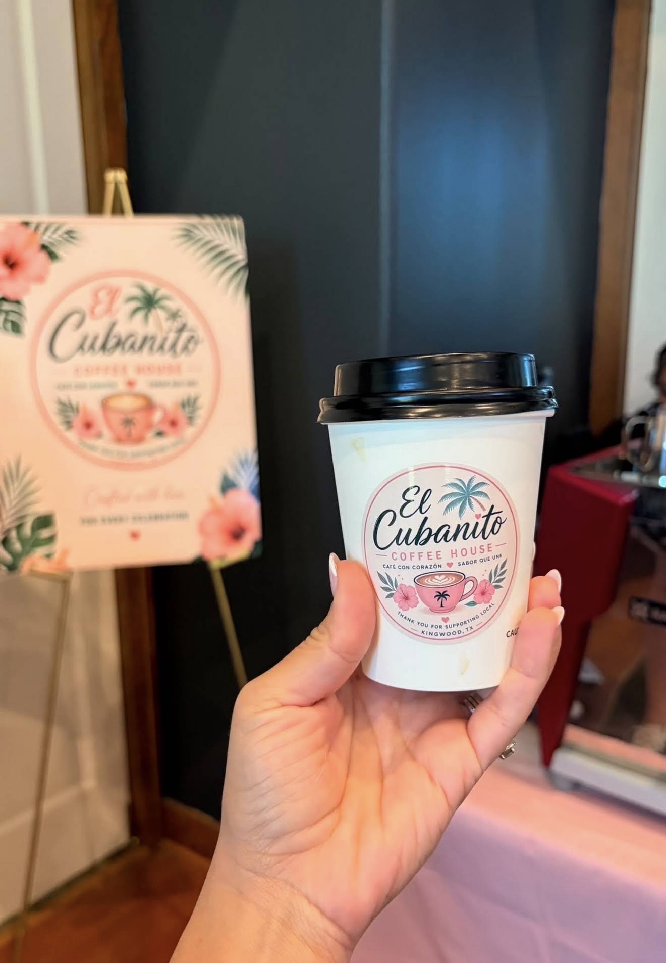 A hot El Cubanito coffee held up beside the menu